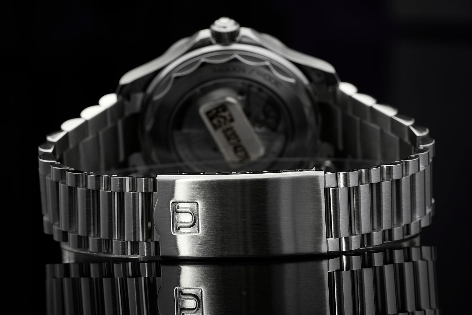 Stainless steel metal bracelet watch with digital display and fold-over clasp, rear view on black background