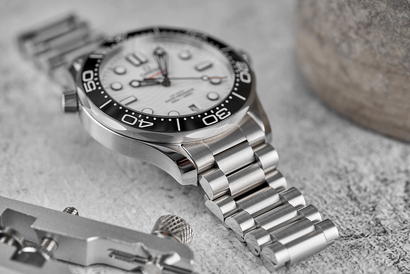 Stainless steel dive watch with white dial, black bezel, and matching metal bracelet on gray surface