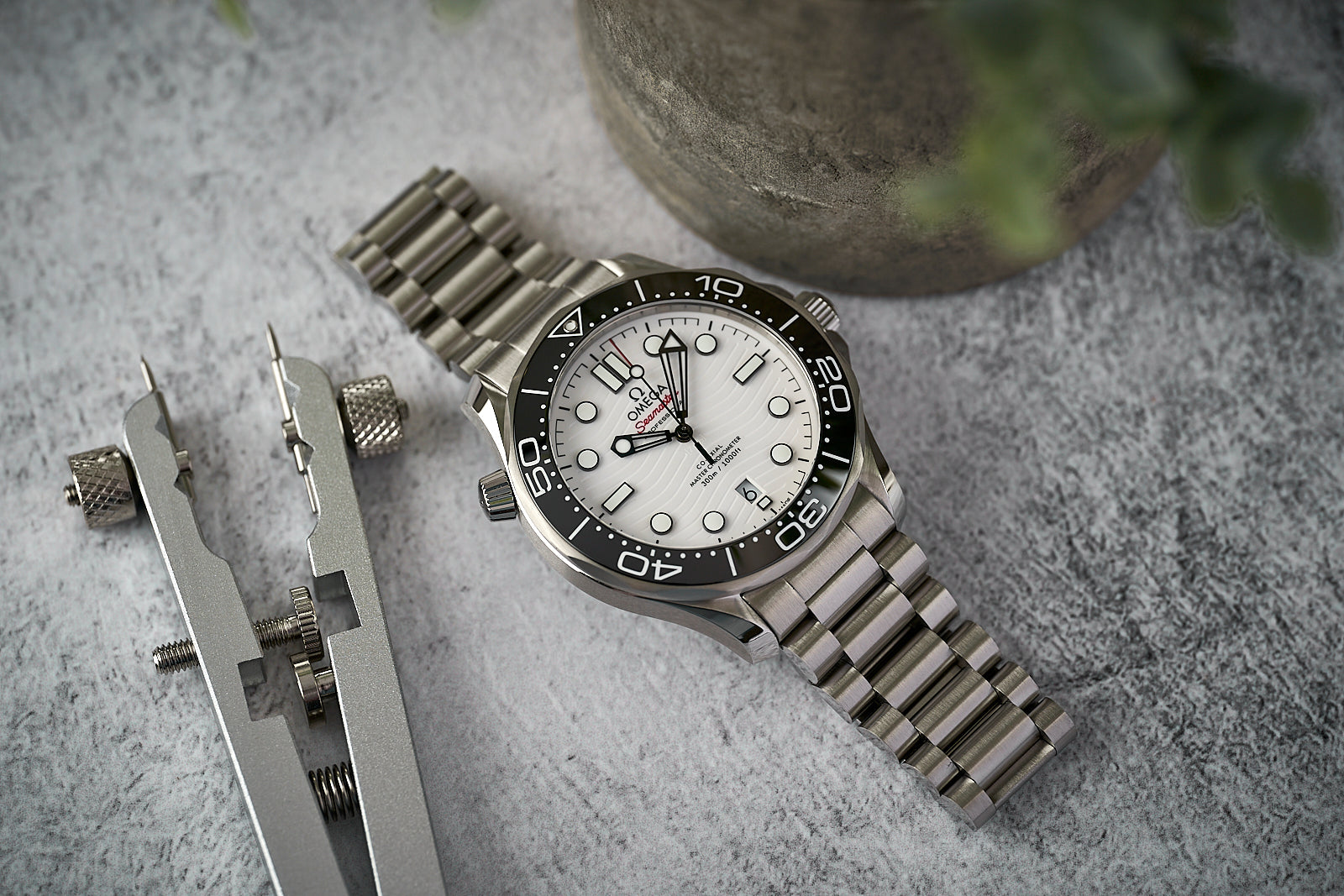 Stainless steel dive watch with white dial and black bezel next to watch adjustment tools on concrete surface