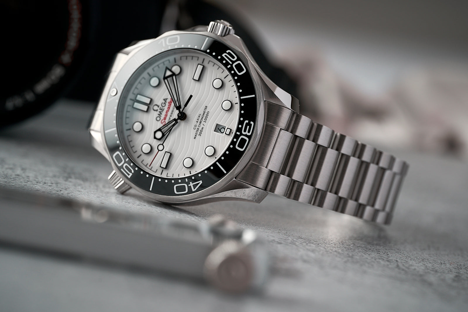 Omega Seamaster 300m stainless steel dive watch with black bezel, silver dial, and matching metal bracelet on gray surface