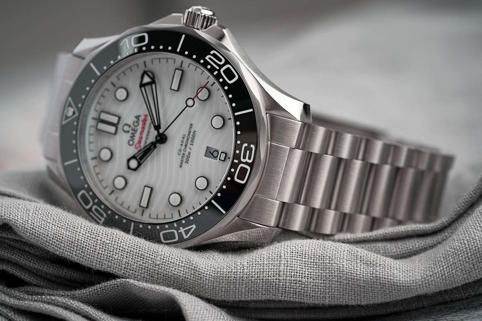 Omega Seamaster 300M professional dive watch with stainless steel bracelet, white dial, black bezel, and luminous hands on fabric background