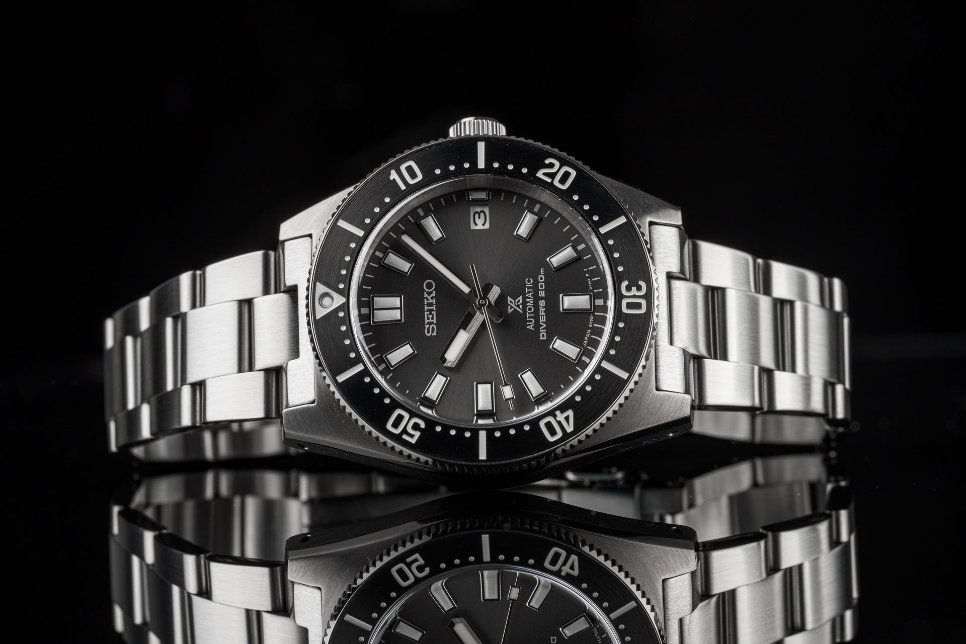 Seiko Prospex automatic diver watch with stainless steel bracelet, black dial, and rotating bezel on reflective surface