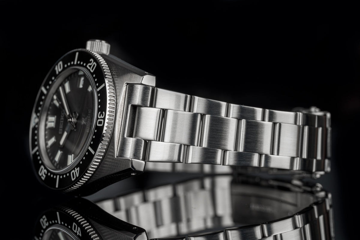 Stainless steel dive watch with black dial, rotating bezel, and matching metal bracelet on black background