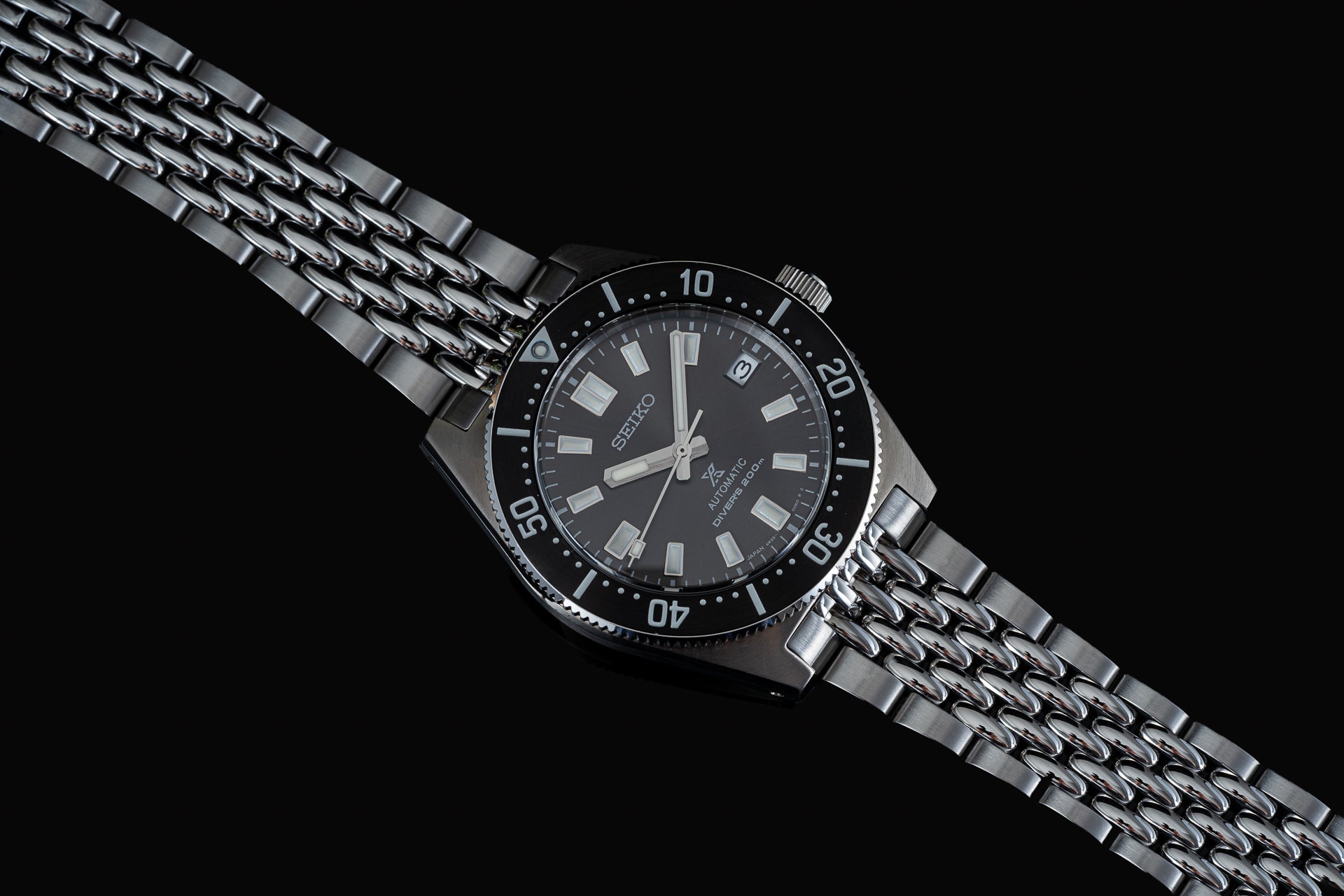 Seiko stainless steel diver watch with black dial, bezel, and beads of rice bracelet on black background