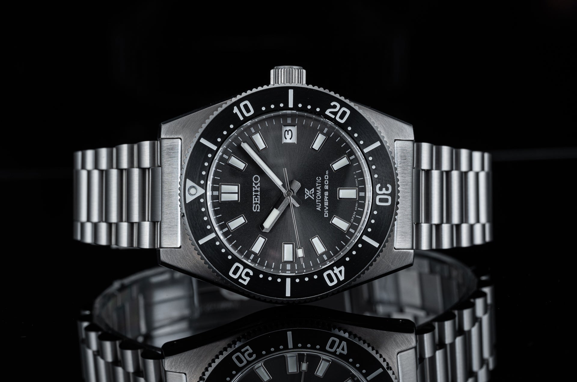 Seiko Prospex automatic diving watch with black dial, stainless steel bracelet and rotating bezel against reflective black background
