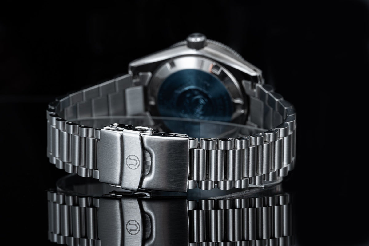 Stainless steel bracelet watch with blue sunburst dial, polished metal three-link band and push-button clasp on black background