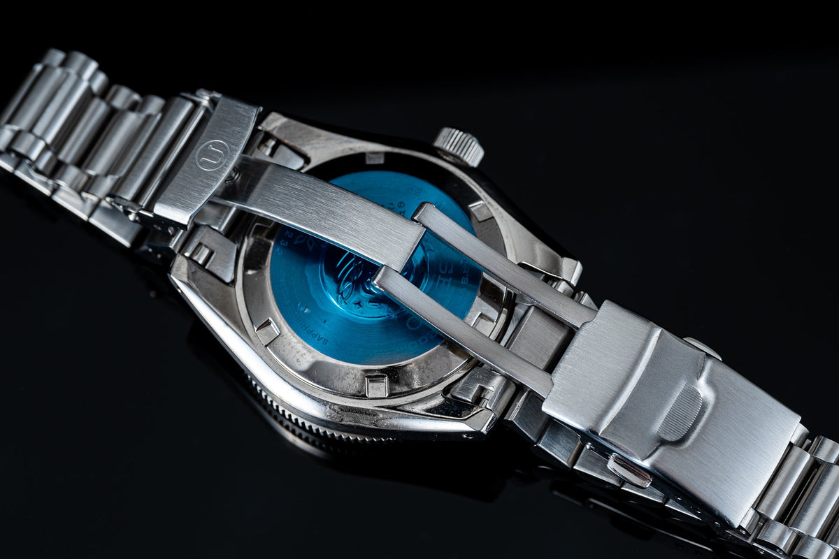 Stainless steel automatic dive watch with bright blue dial and matching metal bracelet, displayed against black background