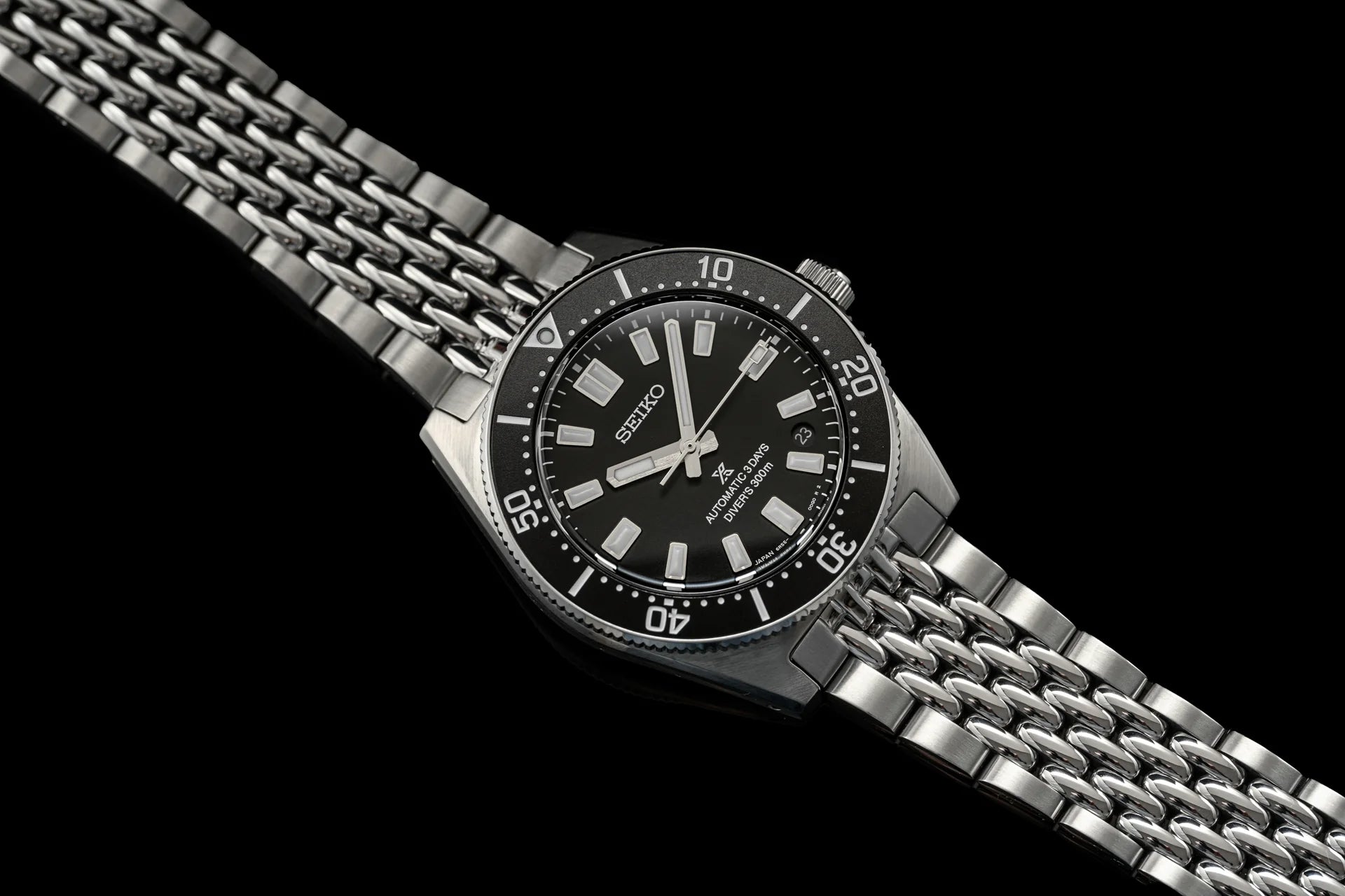 Seiko 5 Sports automatic diving watch with black dial, stainless steel beads of rice bracelet, and rotating bezel on black background