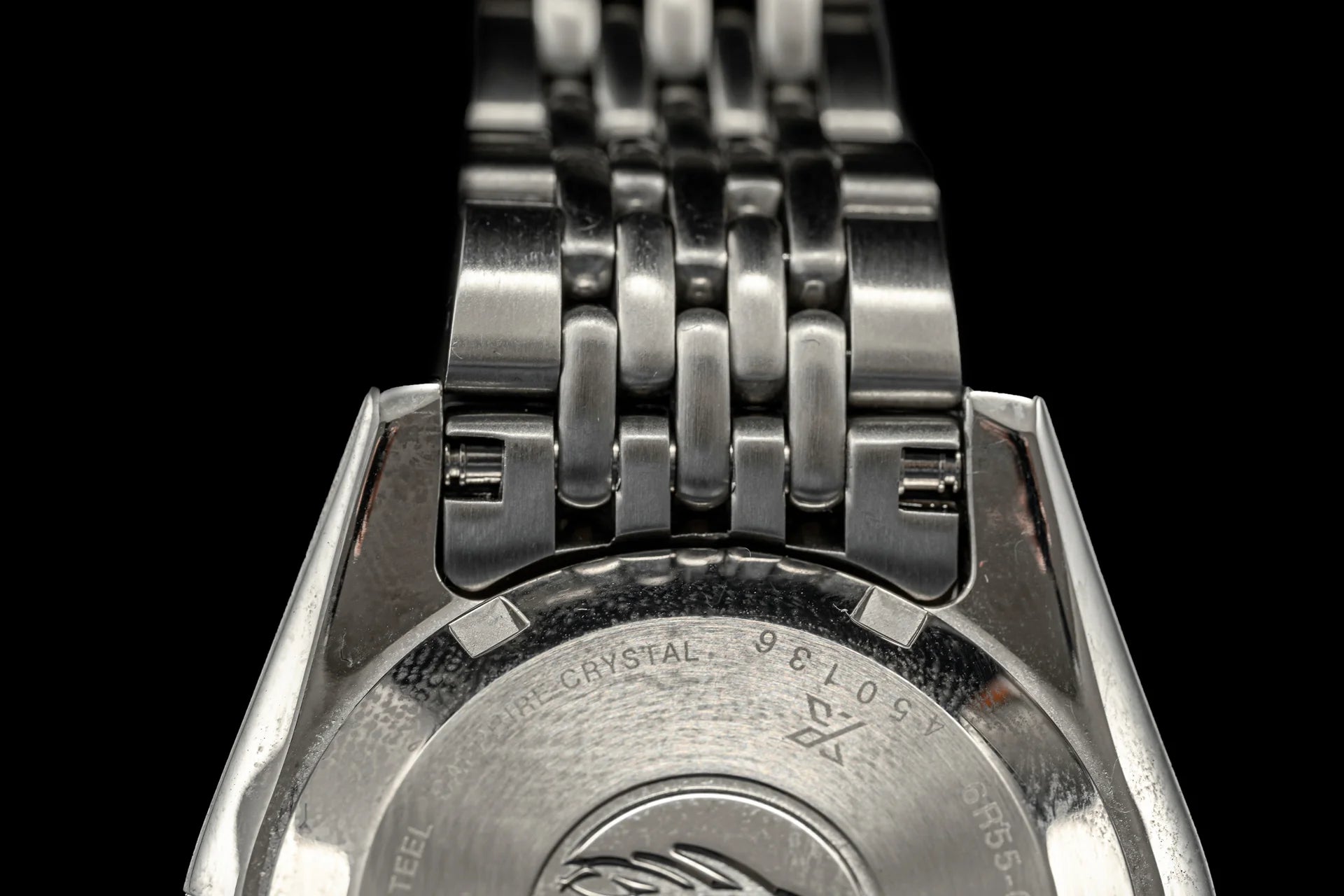 Stainless steel beads of rice bracelet with polished links on Seiko dive watch, overhead view on black background