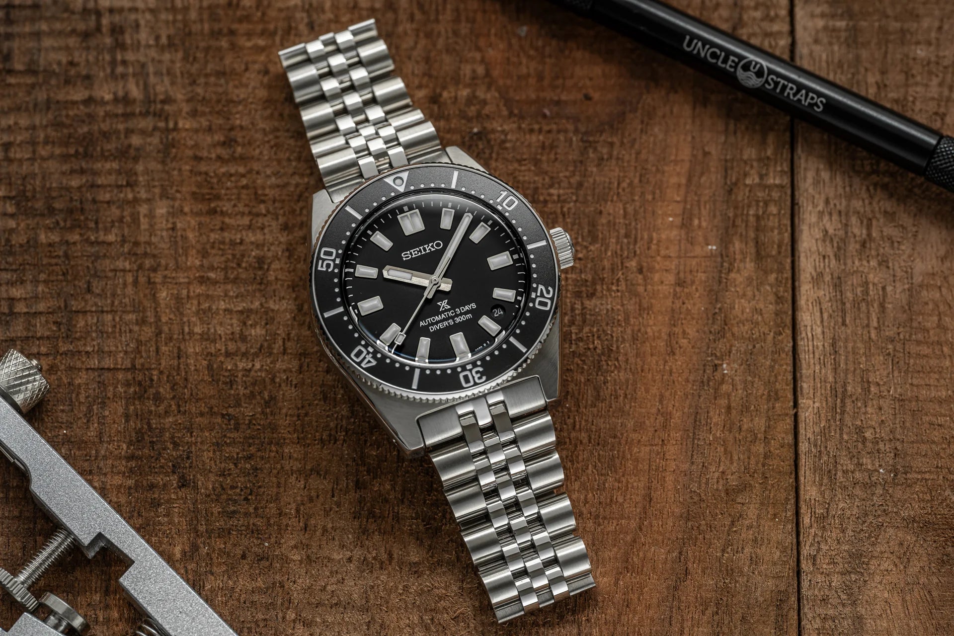 Seiko SPB45 automatic dive watch with stainless steel bracelet on wooden surface next to watch strap