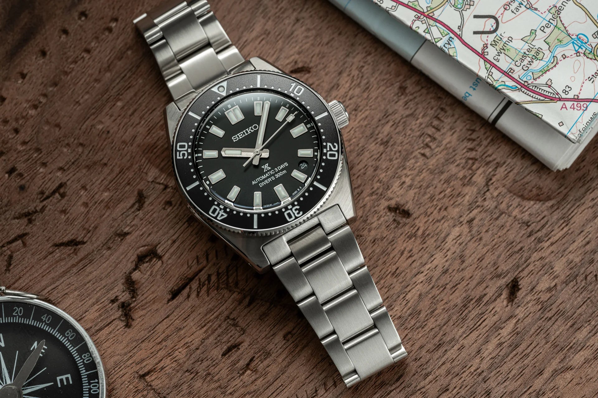 Seiko Prospex automatic diving watch with black dial, stainless steel bracelet, and rotating bezel on wooden surface with map