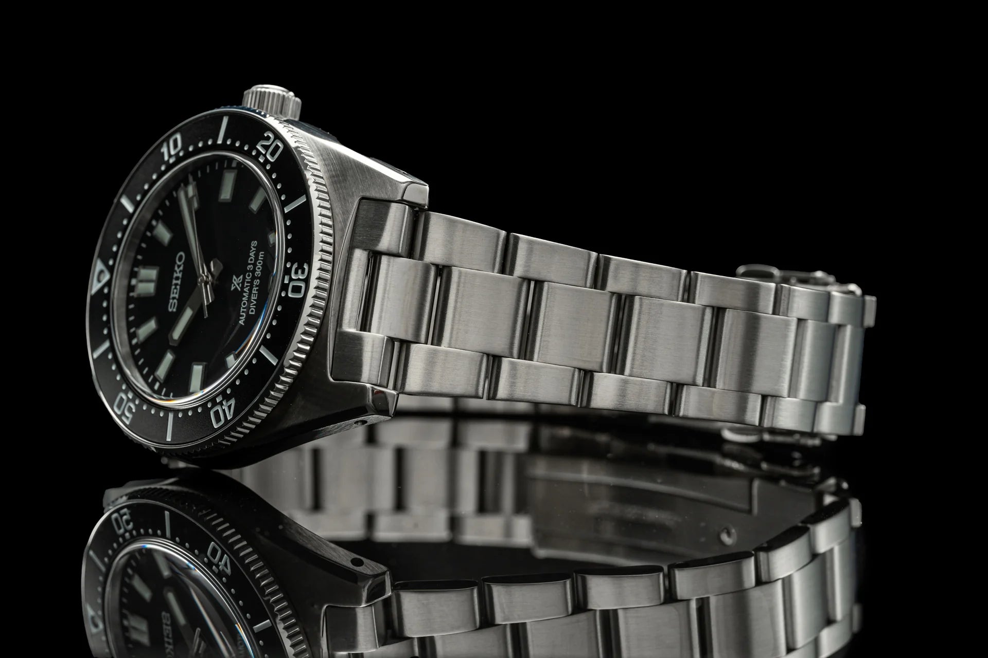 Seiko Prospex diver watch with stainless steel bracelet, black dial and rotating bezel on reflective surface
