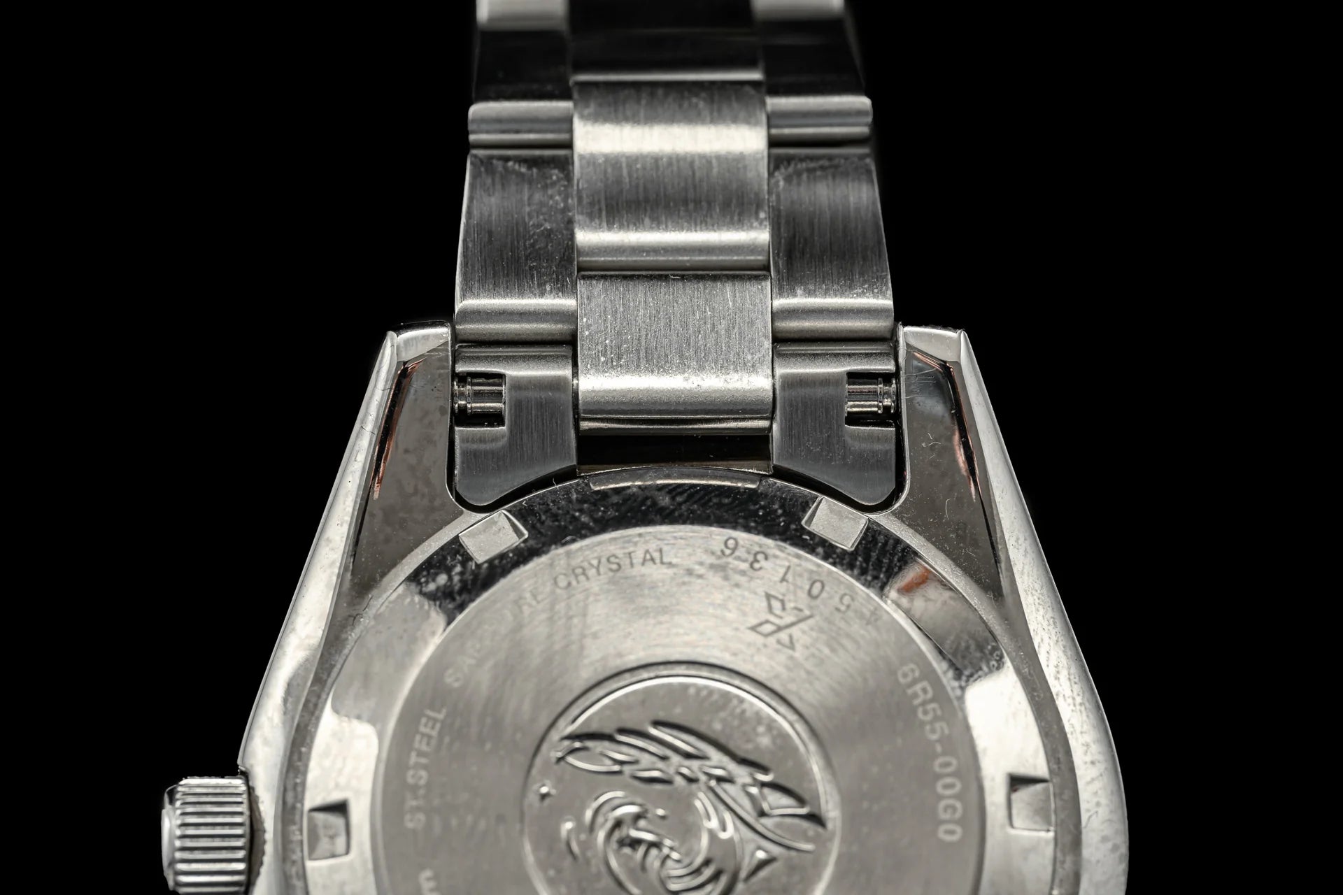 Stainless steel watch caseback with military insignia and sapphire crystal, attached to brushed metal bracelet