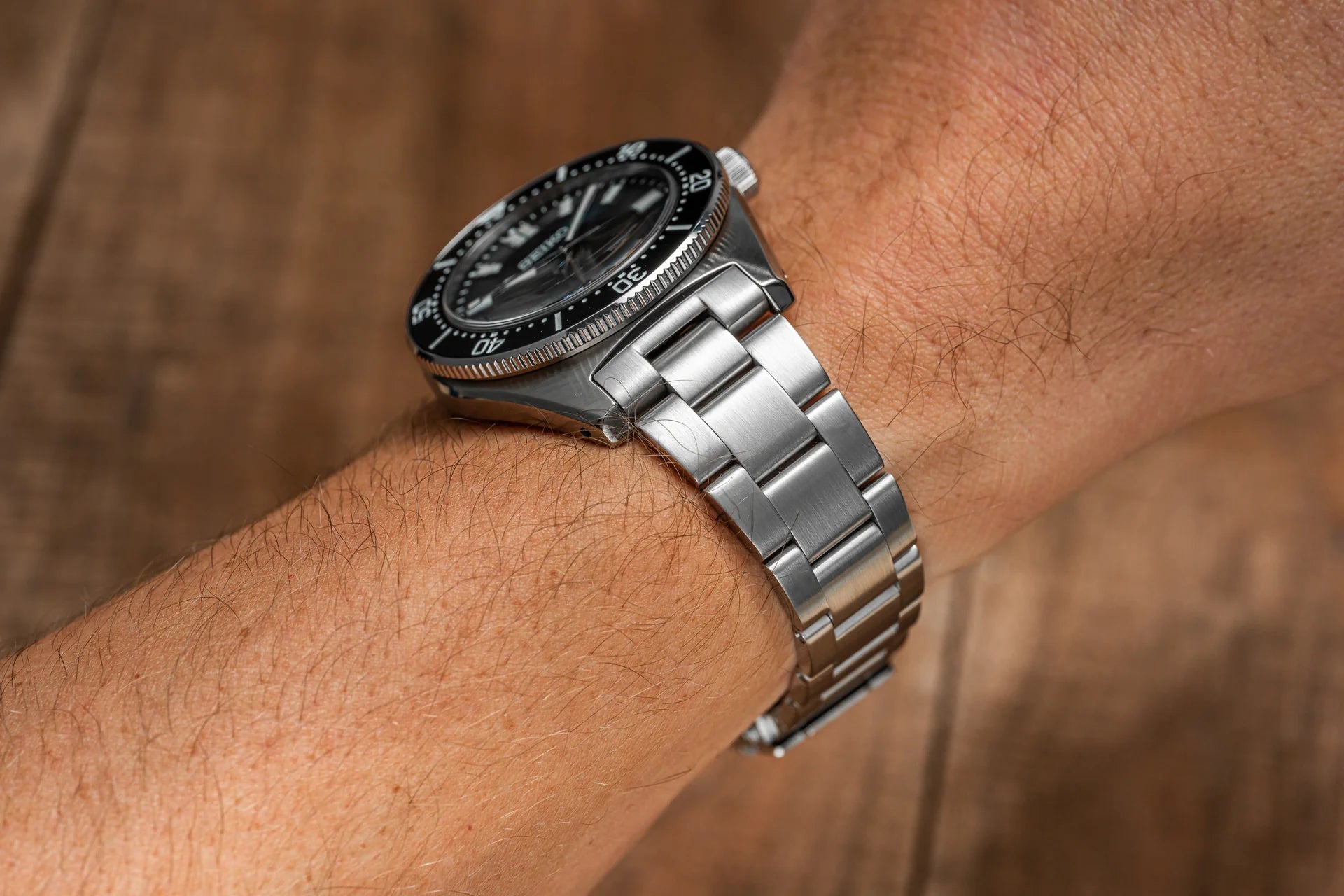 Men's dive watch with black dial and rotating bezel on stainless steel bracelet worn on wrist