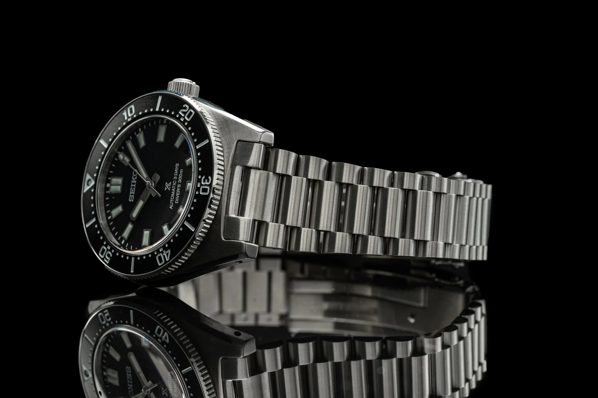 Seiko SPB45x dive watch with black dial and stainless steel bracelet on reflective surface