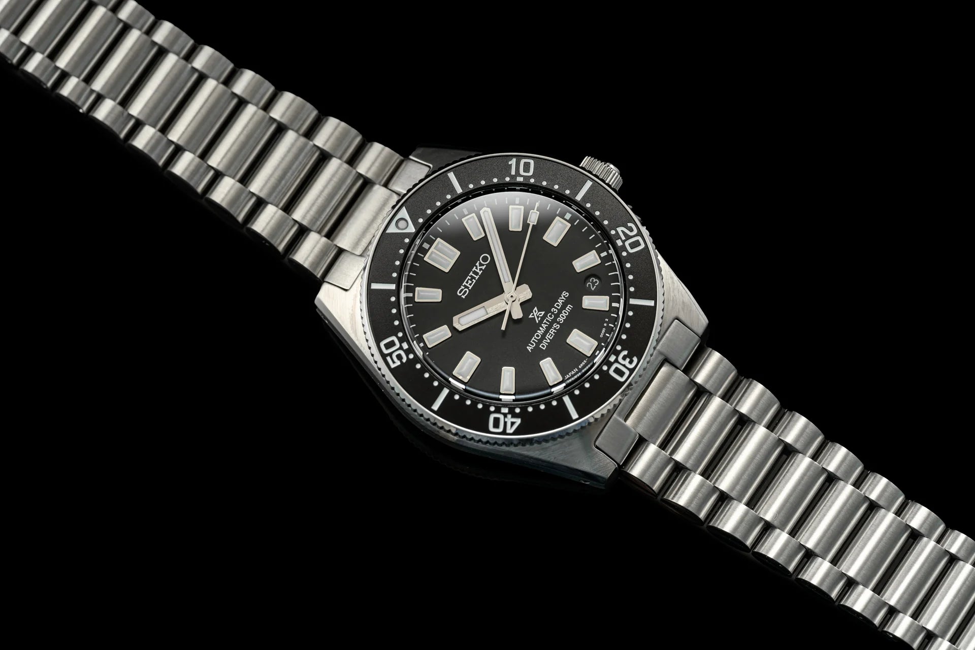 Seiko Prospex stainless steel diver watch with black dial, silver hour markers, rotating bezel, and matching metal bracelet on black background