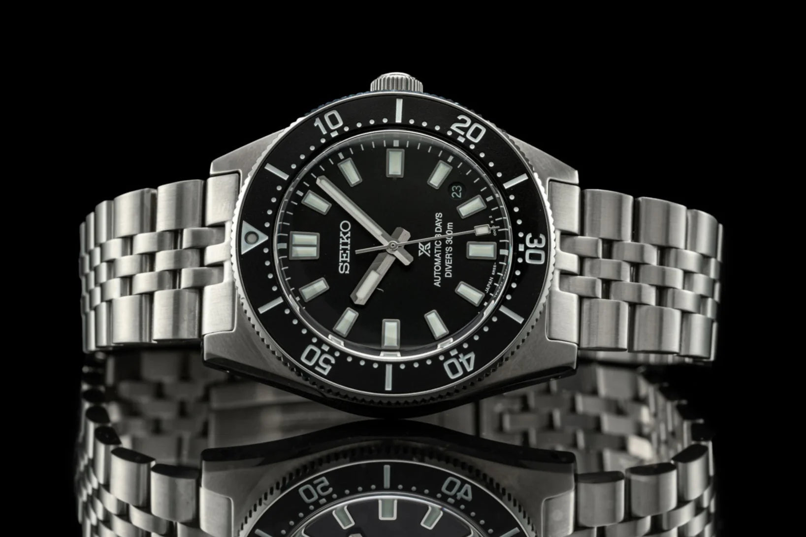 Seiko SPB45x automatic dive watch with stainless steel bracelet, black dial, and rotating bezel on reflective surface