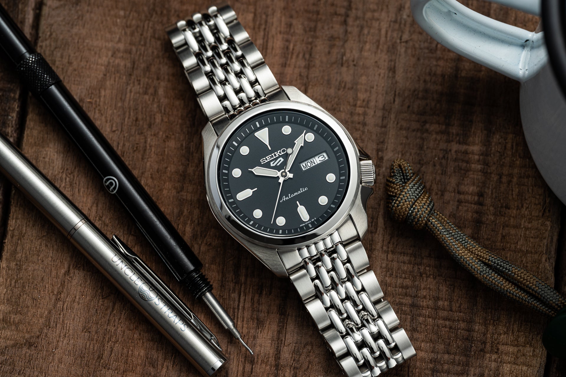 Seiko automatic watch with black dial and stainless steel bracelet on wooden desk with accessories