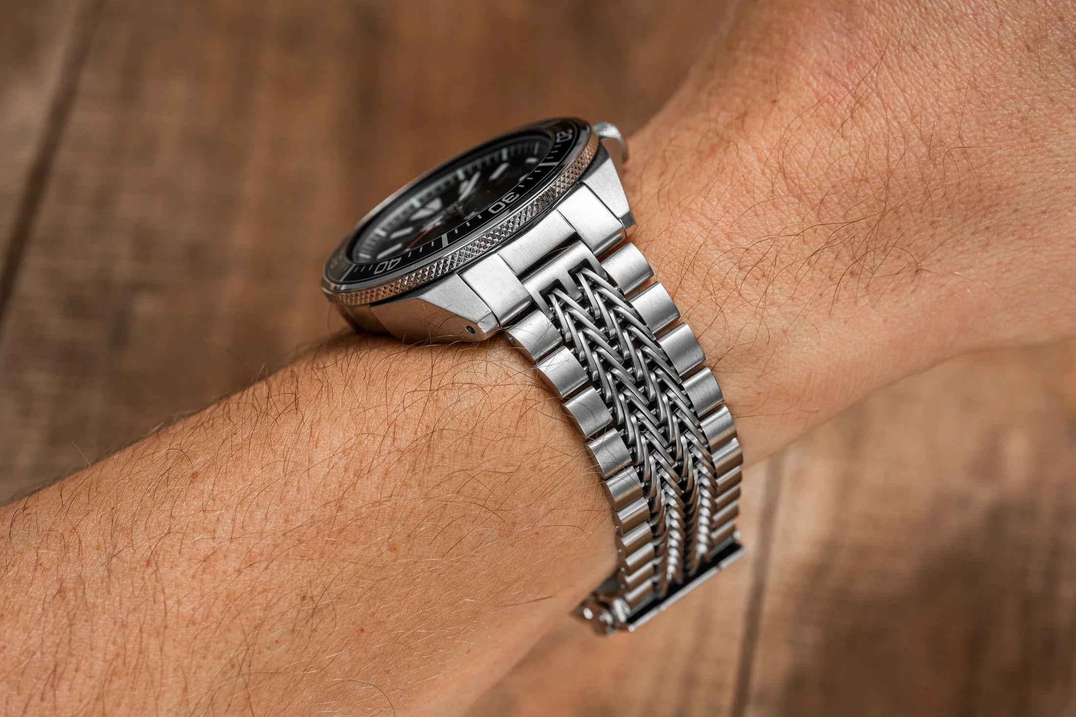 Silver stainless steel dive watch with black dial and rope-textured bracelet worn on wrist