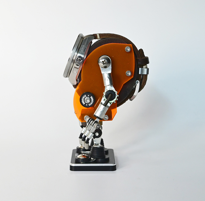 Orange minibot robot watch stand with articulated arms holding timepiece on black base