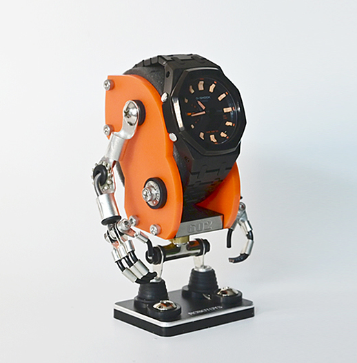 Orange minibot watch stand with black analog watch, metallic robot arms, and black base