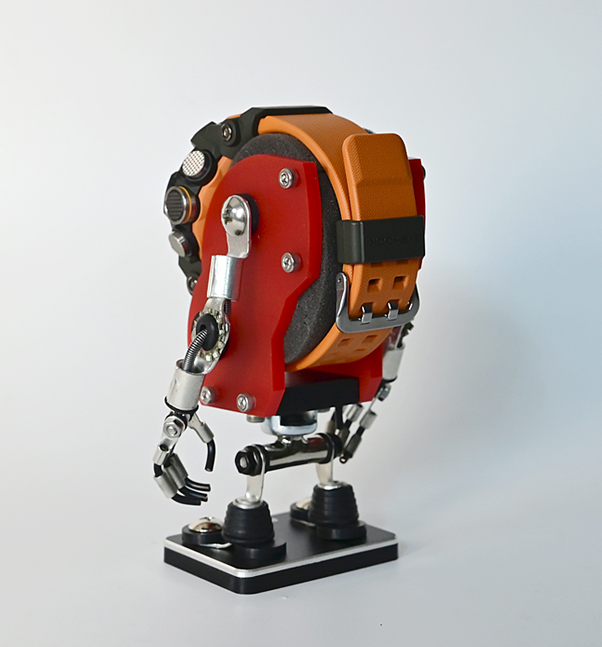 Red and orange miniature robot watch stand with articulated limbs and mechanical details on display base
