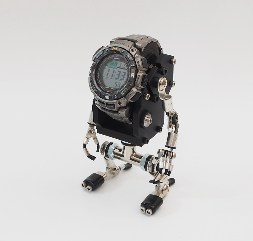 Miniature robot watch stand with black body, articulated silver metal limbs and feet, digital watch mounted on chest display