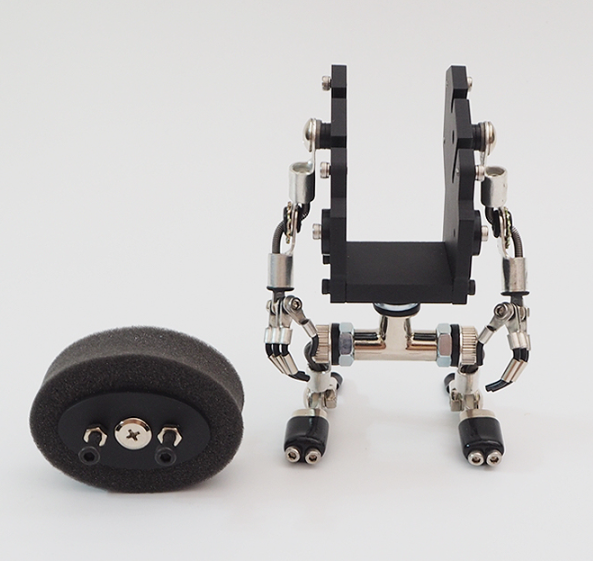 Black MiniMech robot watch stand with articulated metal arms and legs, featuring smartphone holder and accessory storage