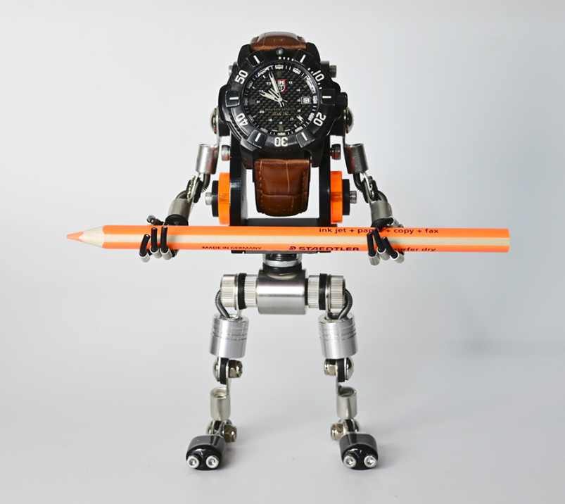 Black RoboMech watch stand holding chronograph timepiece with brown leather strap and orange mechanical arms gripping pencil
