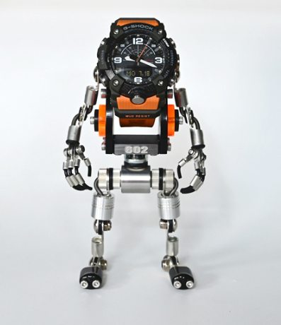 Black and orange digital analog hybrid watch mounted on articulated silver metal robot stand with poseable arms and legs