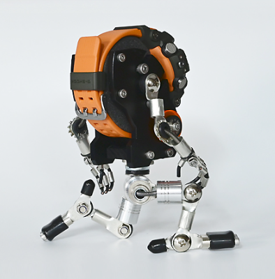 Black and orange robotic figure with articulated metal limbs and mechanical joints, stylized robot toy or watch stand display piece