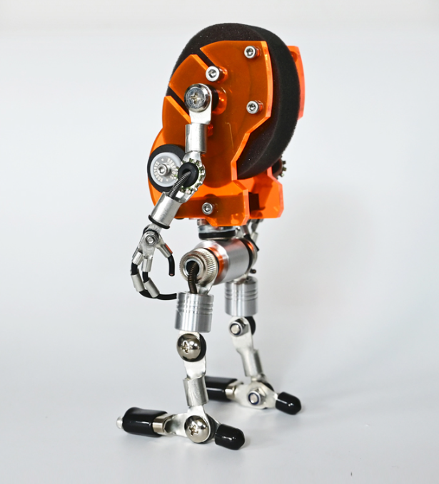 Orange and black robotic watch stand with articulated metal legs and mechanical claw hand display holder