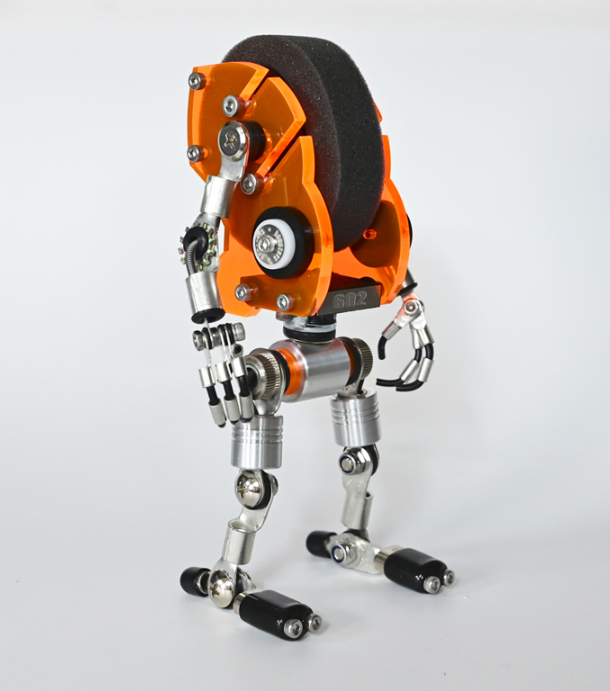 Orange RoboMech watch stand with articulated silver metal limbs and black feet, featuring gear wheel details and mechanical design