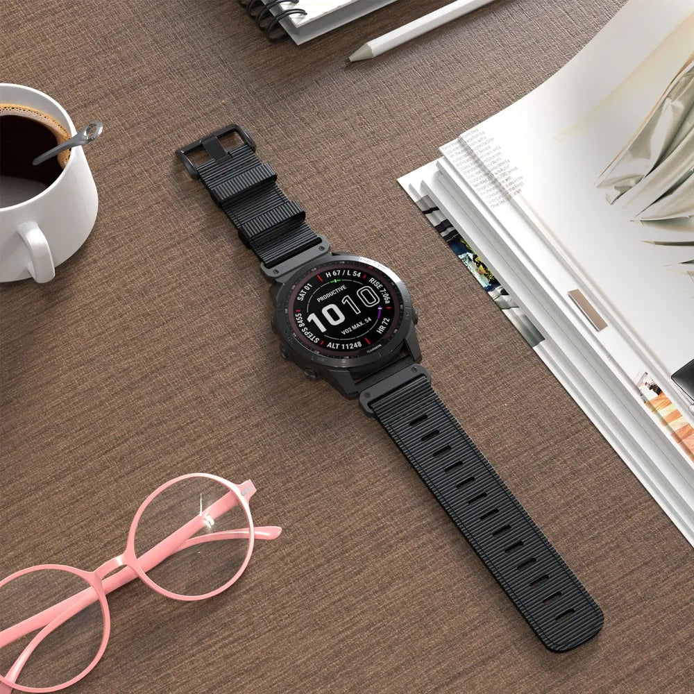 Black tactical smartwatch with digital display and black fabric strap on office desk, surrounded by coffee, notepad and glasses