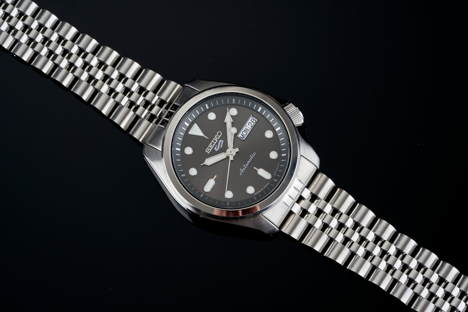 Seiko automatic men's watch with black dial, stainless steel bracelet and case, date window, on dark background