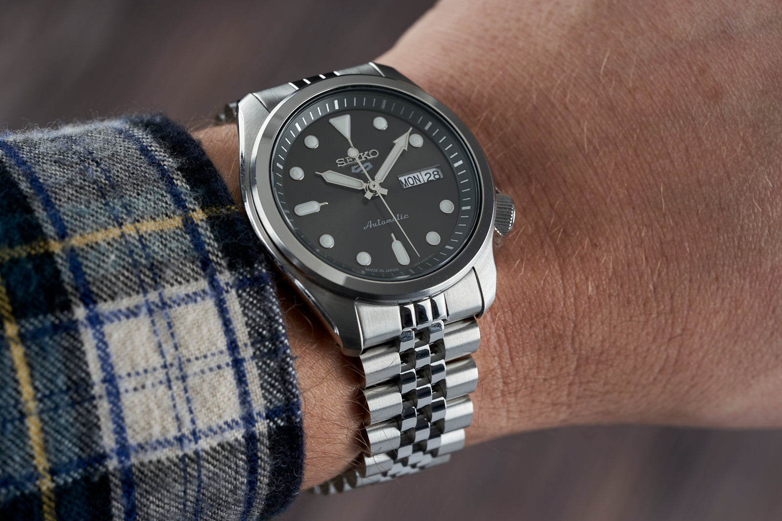 Seiko SRPE automatic watch with black dial and silver steel bracelet on wrist wearing plaid shirt