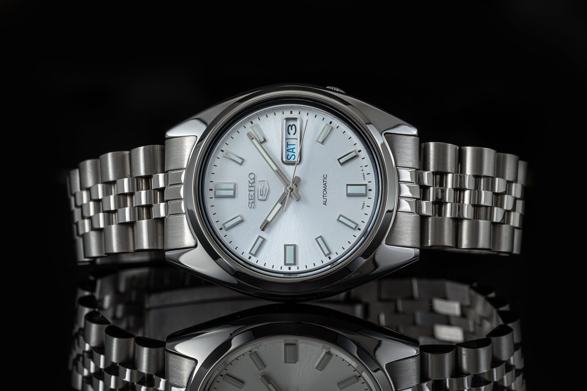 Seiko 5 SNXS automatic watch with silver dial, day-date window, stainless steel bracelet on black background