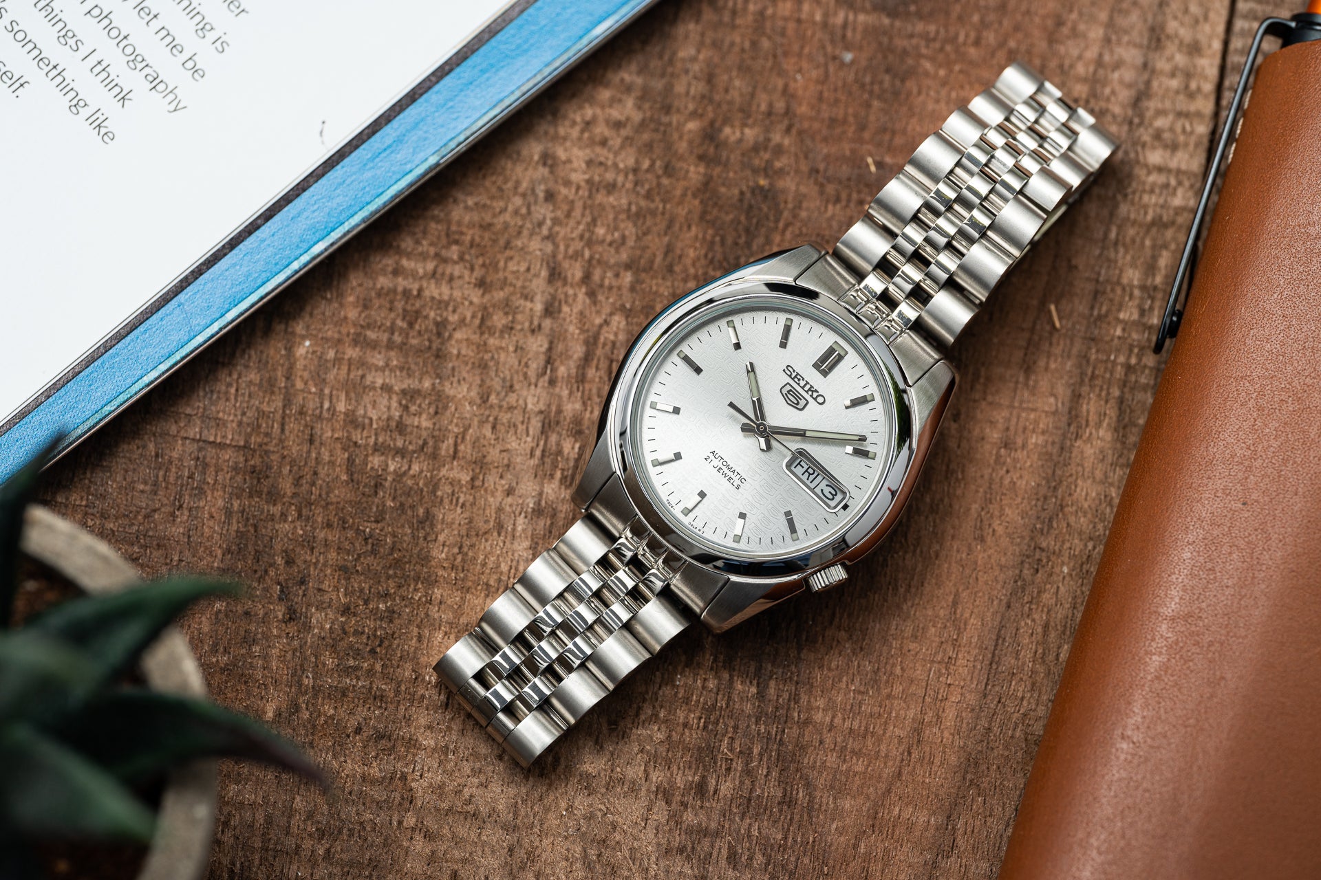 Seiko 5 SNKL stainless steel automatic watch with white dial and day-date display on wooden surface