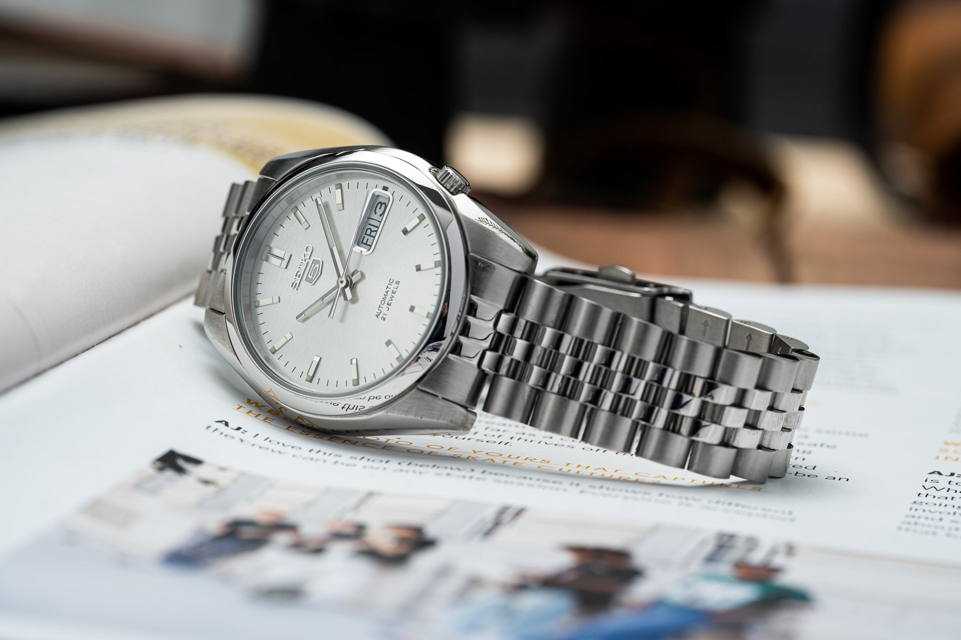Seiko 5 SNKL stainless steel automatic watch with silver dial and day-date window on metal bracelet displayed on newspaper