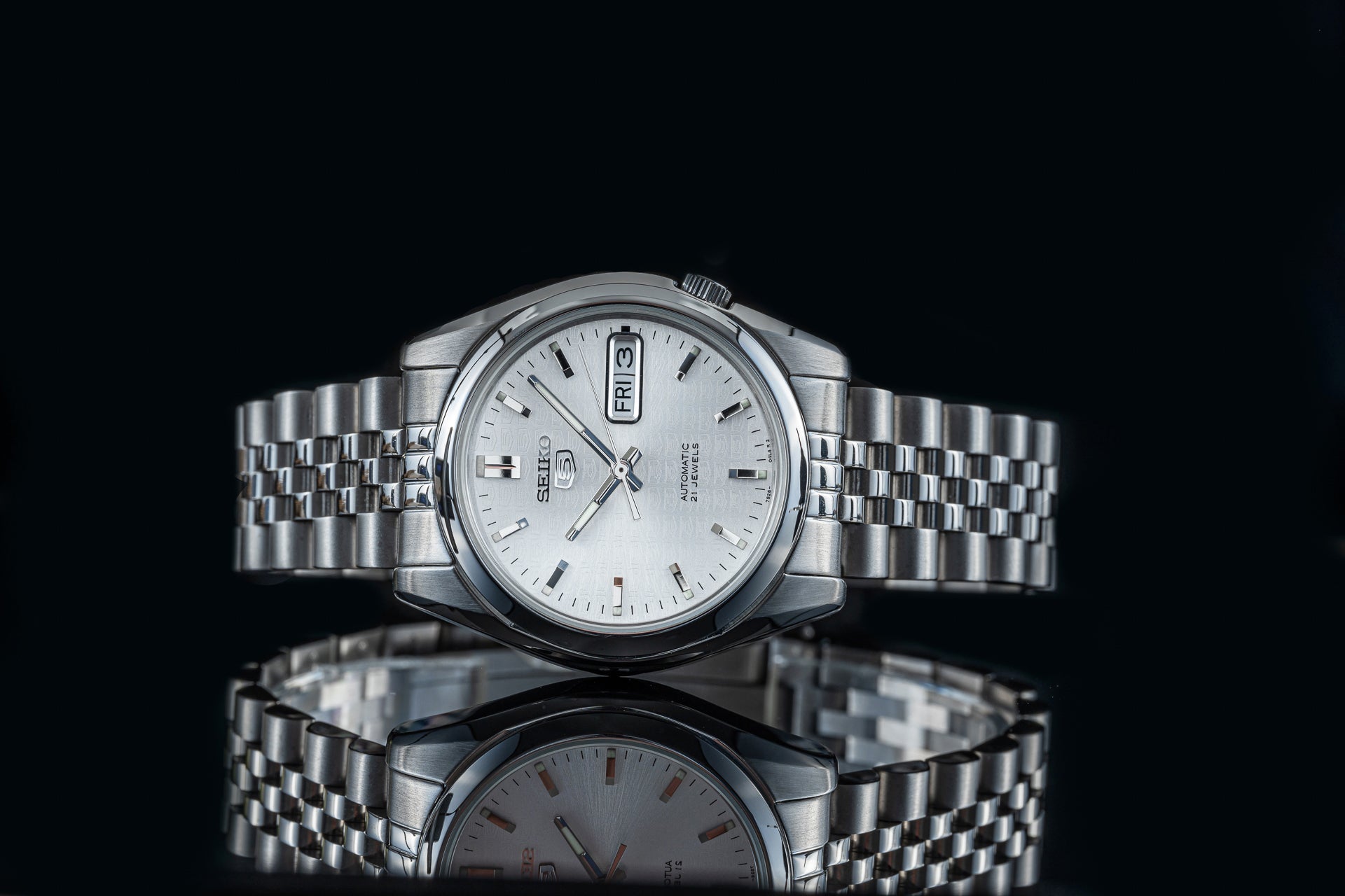 Seiko 5 SNKL automatic stainless steel watch with white dial, day-date display, and metal bracelet on black background