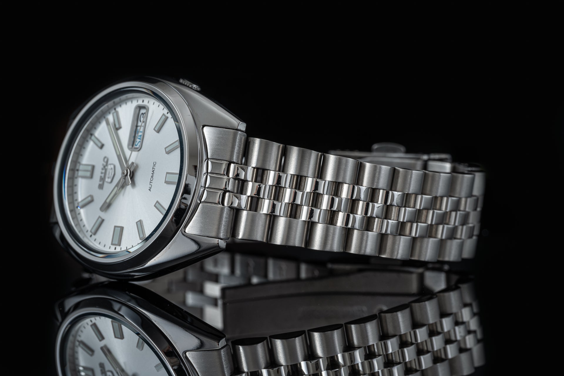 Seiko 5 SNXS automatic stainless steel watch with silver bracelet and white dial on black background