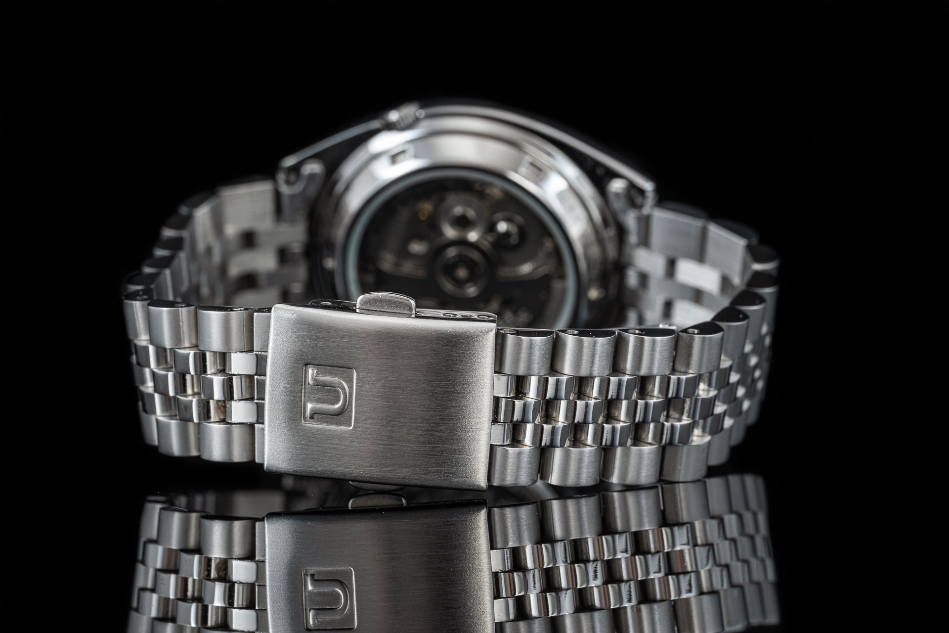 Stainless steel Seiko 5 SNXS watch with military-style bracelet and automatic movement dial against black background