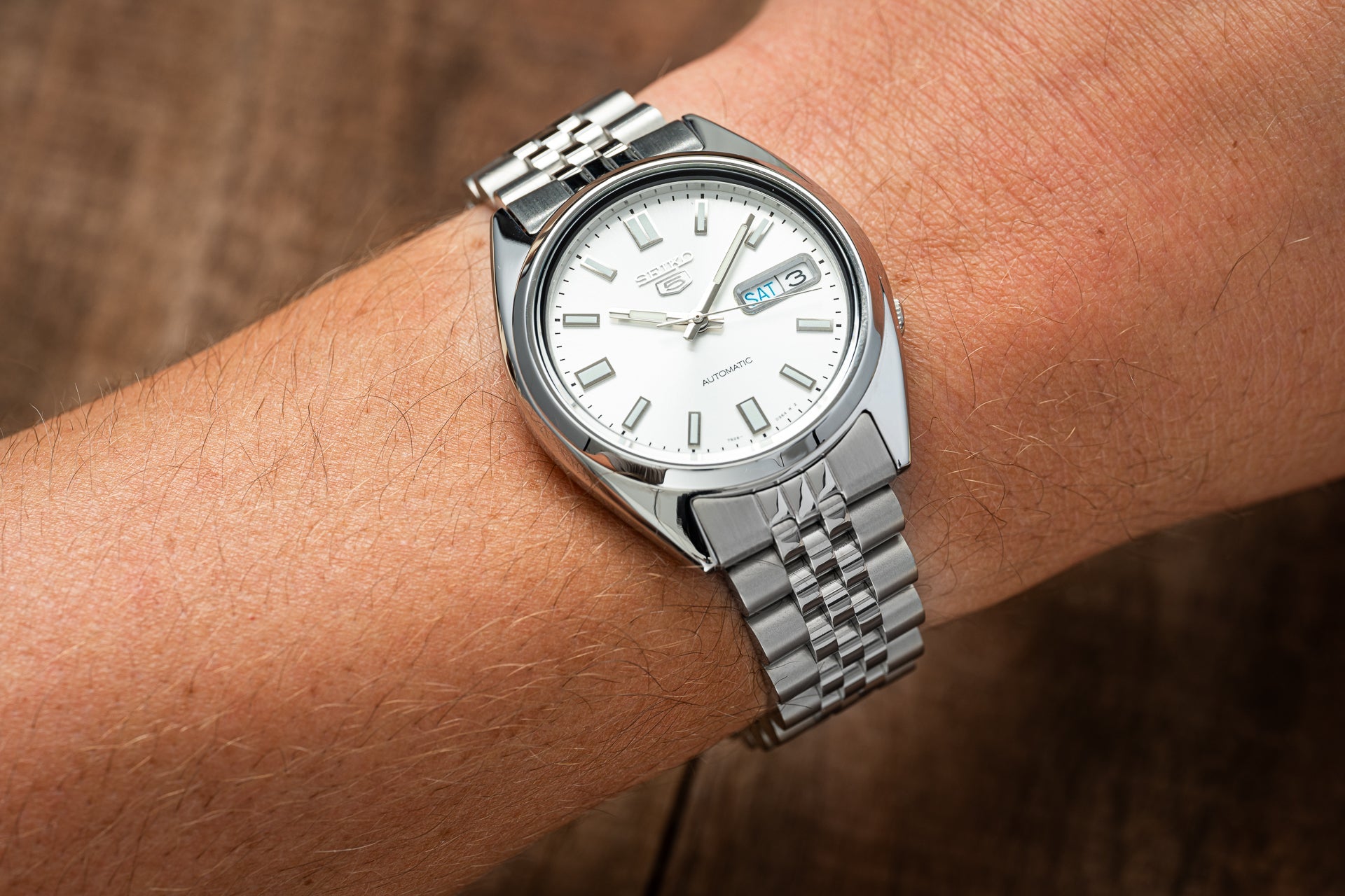 Seiko 5 SNXS automatic watch with white dial and day-date window on stainless steel bracelet worn on wrist