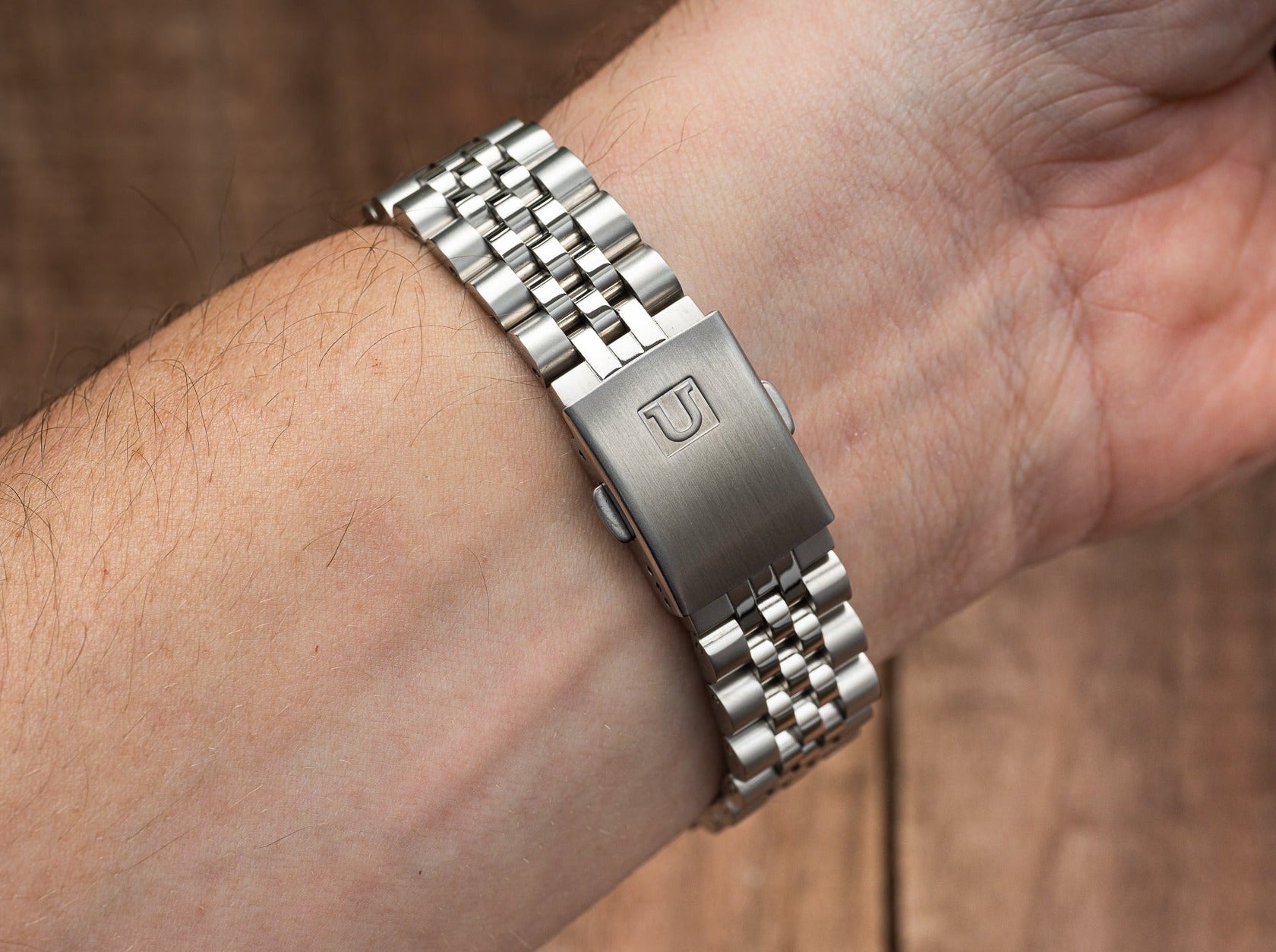 Stainless steel watch bracelet with brushed clasp and polished links on male wrist, classic metal watch band detail