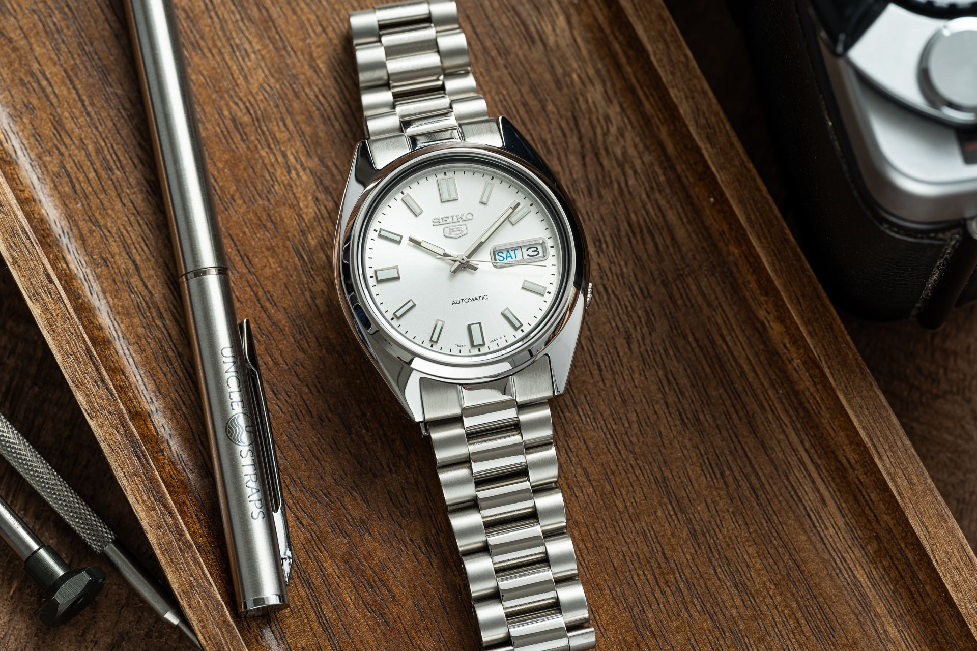Seiko 5 automatic stainless steel watch with white dial and day-date window on wooden desk