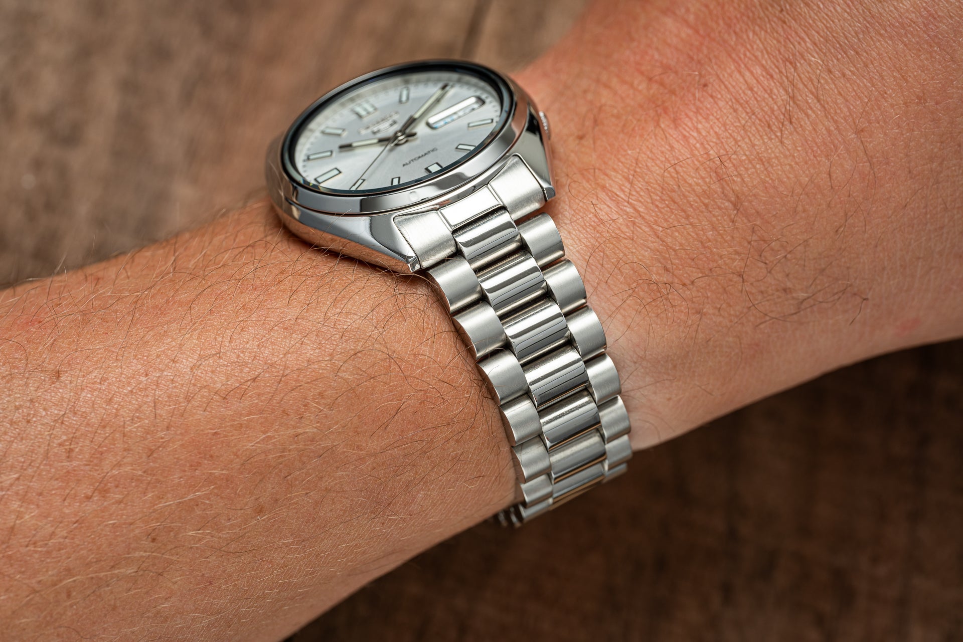 Silver stainless steel automatic watch with white dial worn on wrist, featuring three-link metal bracelet and applied indices