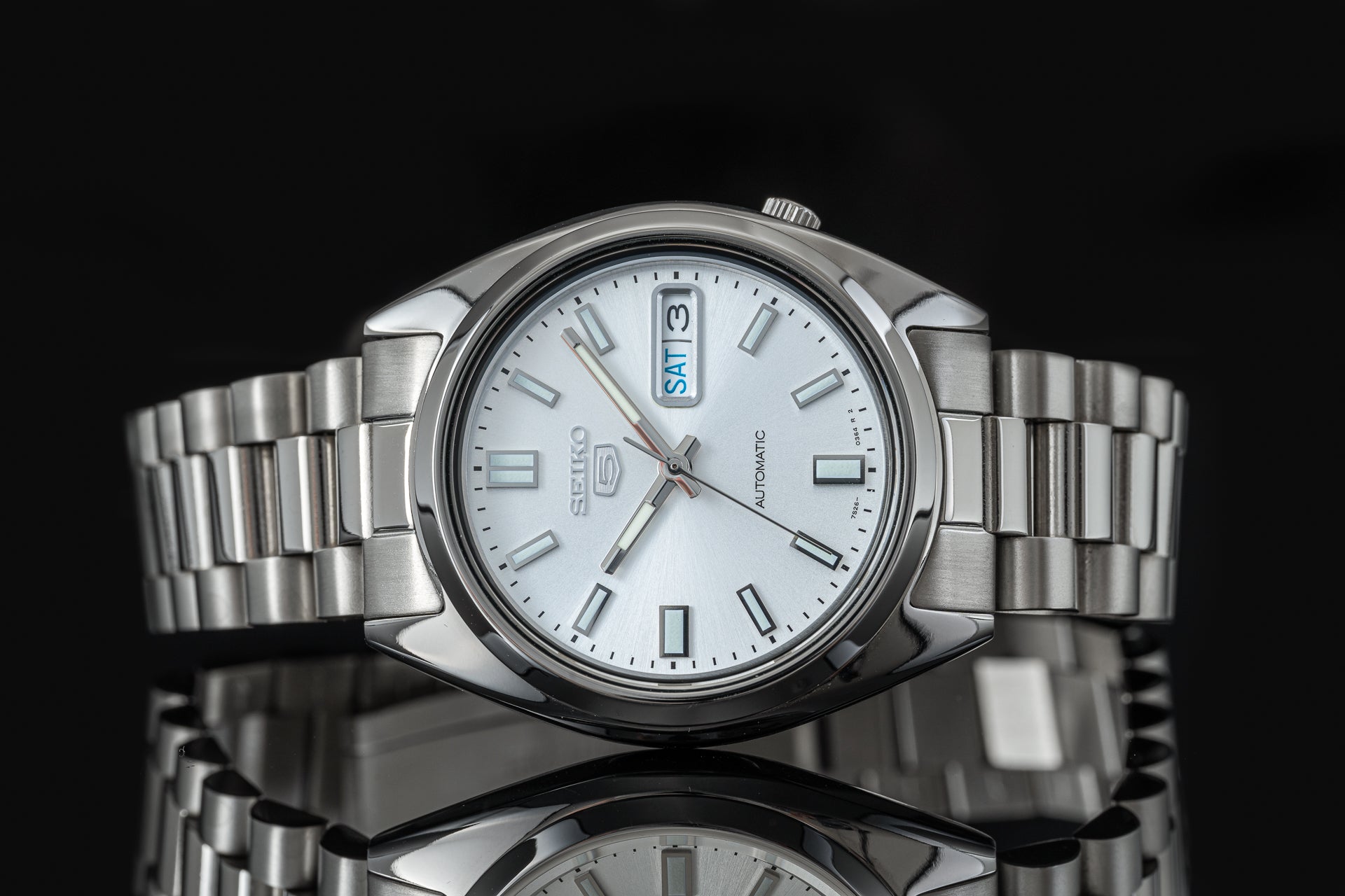 Seiko 5 SNXS automatic stainless steel watch with white dial, day-date window, and matching metal bracelet on black background