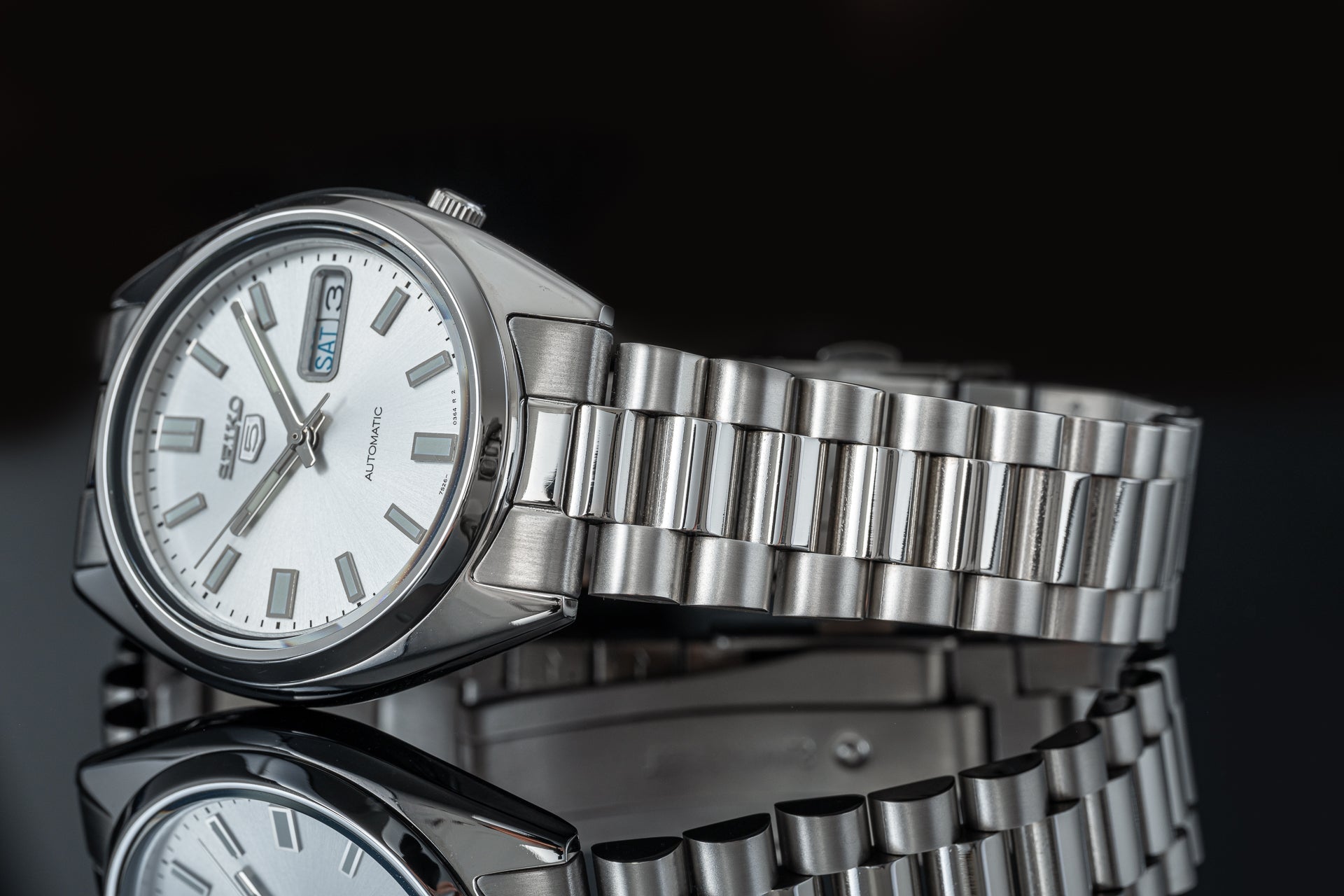 Seiko 5 SNXS automatic stainless steel watch with white dial and matching metal bracelet on black background