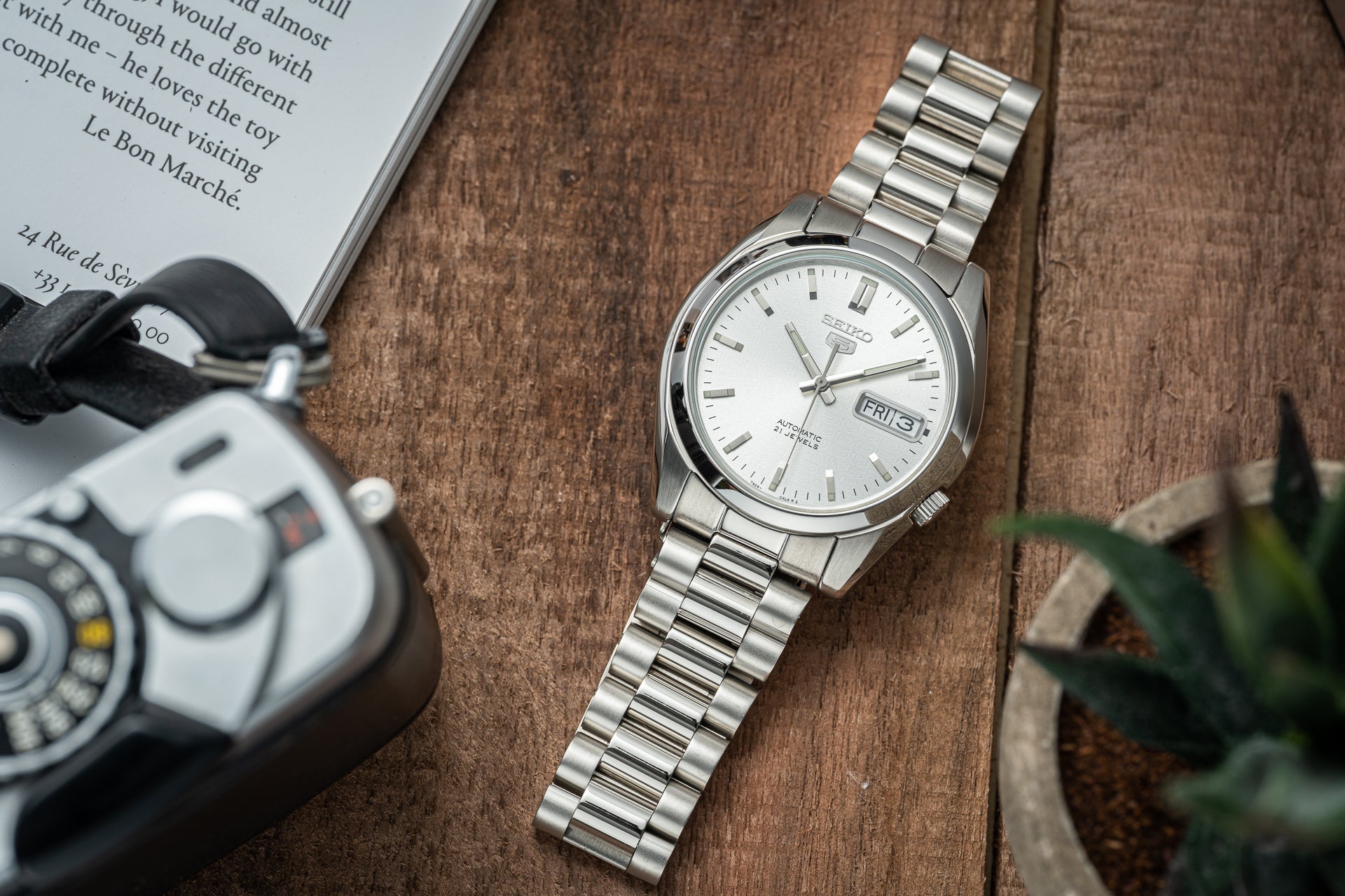 Seiko 5 automatic stainless steel watch with white dial and day-date display on wooden surface