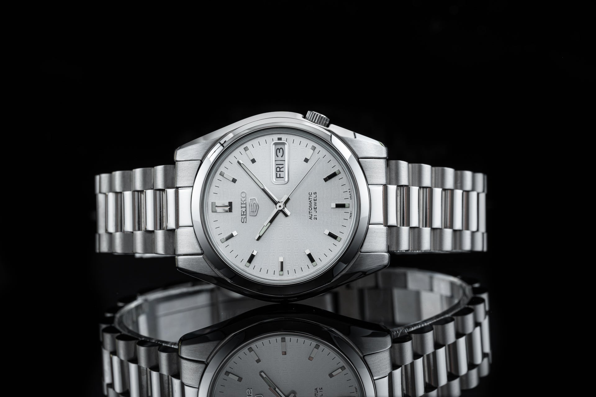 Seiko 5 SNKL automatic stainless steel watch with day-date window, silver dial, and matching metal bracelet on black background